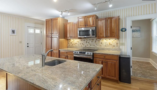 kitchen featuring light stone counters, brown cabinets, stainless steel appliances, a sink, and wallpapered walls