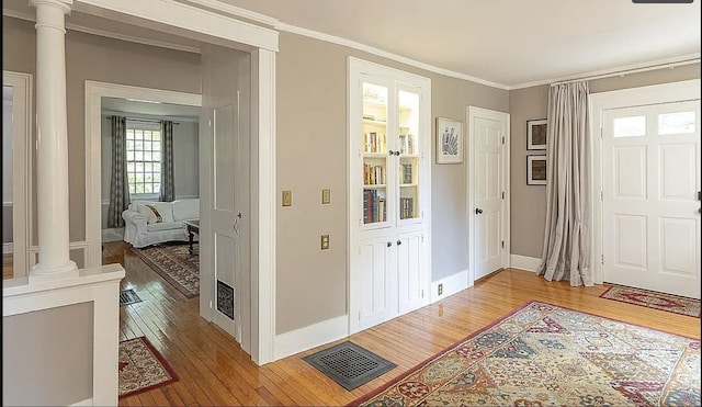 entrance foyer featuring light wood-style floors, visible vents, decorative columns, and ornamental molding