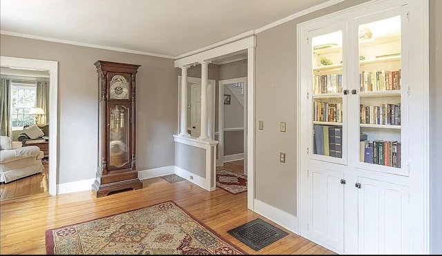 interior space with decorative columns, crown molding, baseboards, and wood finished floors