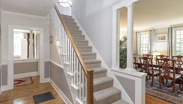 stairway with decorative columns, visible vents, wood finished floors, and ornamental molding