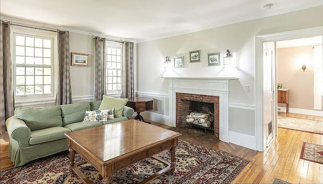 living room featuring baseboards, hardwood / wood-style floors, a fireplace with flush hearth, and crown molding