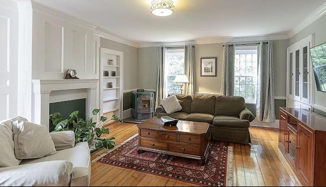 living room featuring built in features, a wood stove, crown molding, and light wood-style flooring