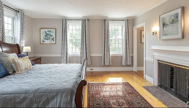 bedroom featuring a fireplace with flush hearth, multiple windows, crown molding, and light wood-style flooring