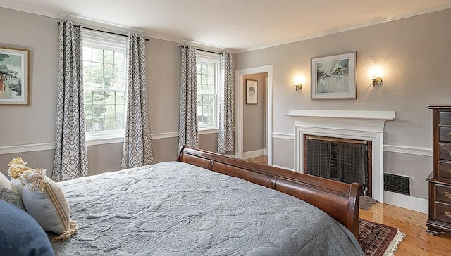 bedroom featuring baseboards, visible vents, ornamental molding, wood finished floors, and a fireplace