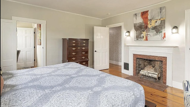 bedroom featuring a fireplace with flush hearth, baseboards, wood finished floors, and crown molding