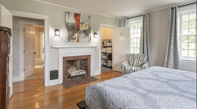 bedroom featuring hardwood / wood-style flooring, a fireplace with flush hearth, and crown molding