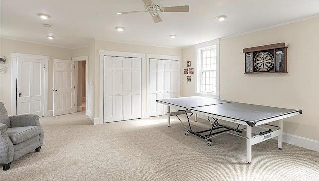 game room featuring a ceiling fan, baseboards, crown molding, and light colored carpet