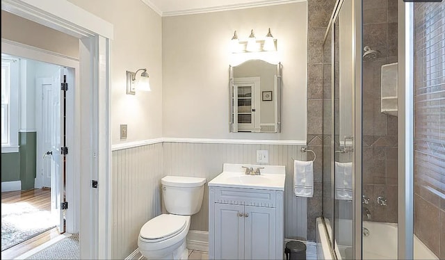 bathroom featuring toilet, shower / bath combination with glass door, vanity, wainscoting, and crown molding