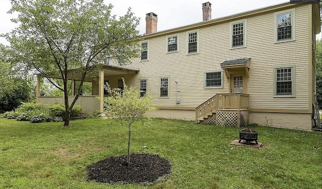 back of property with an outdoor fire pit, a chimney, and a lawn