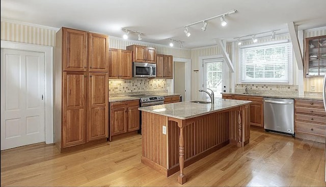 kitchen with light stone counters, brown cabinets, stainless steel appliances, light wood-style floors, and a sink