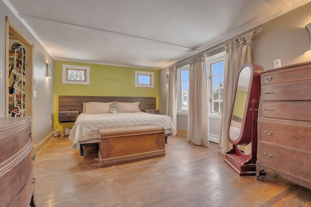 bedroom with a baseboard radiator, crown molding, baseboards, and wood finished floors