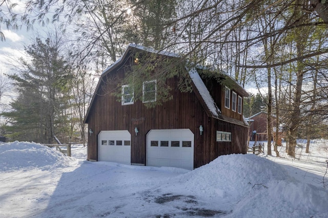 snow covered property with a detached garage and a gambrel roof