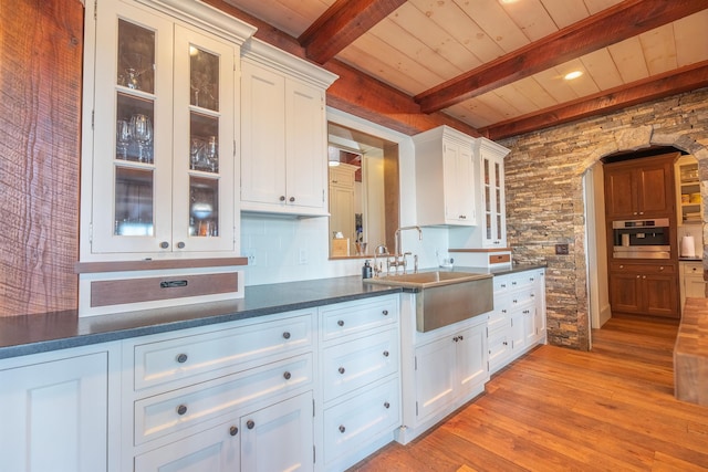 kitchen with light wood-style flooring, stainless steel oven, white cabinets, and a sink