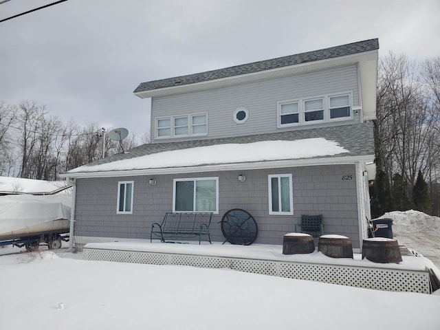 snow covered back of property with roof with shingles