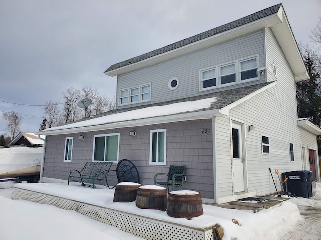 snow covered rear of property featuring roof with shingles