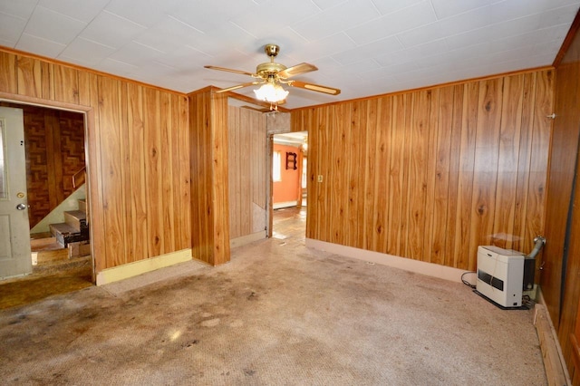 spare room featuring carpet floors, a ceiling fan, wood walls, baseboards, and stairs