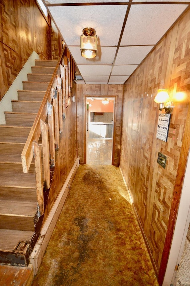 hall featuring stairway, a paneled ceiling, and wooden walls