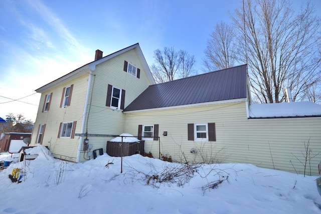 snow covered back of property with metal roof and a chimney