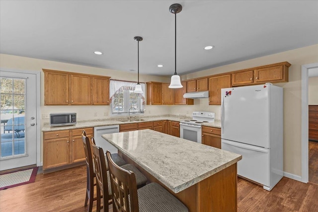 kitchen with appliances with stainless steel finishes, dark wood-type flooring, light countertops, under cabinet range hood, and a sink