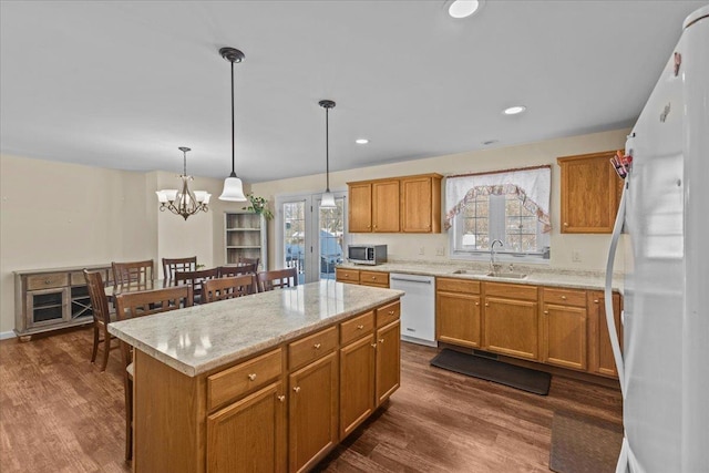 kitchen featuring white appliances, dark wood finished floors, a center island, pendant lighting, and a sink