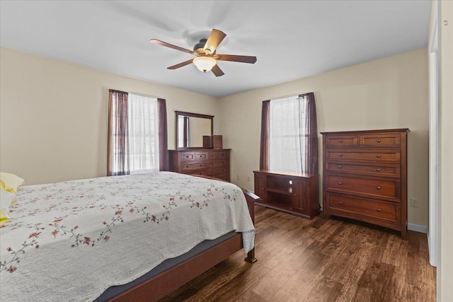 bedroom featuring multiple windows, dark wood-style flooring, a ceiling fan, and baseboards