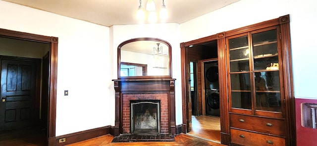 interior space with a brick fireplace, wood finished floors, and stacked washer and clothes dryer