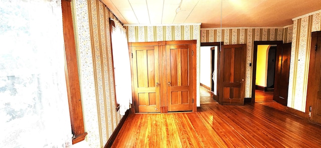 unfurnished bedroom featuring ornamental molding, wood finished floors, and wallpapered walls