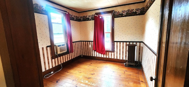 empty room with hardwood / wood-style floors, wainscoting, cooling unit, baseboards, and wallpapered walls