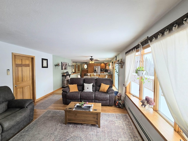 living room featuring light wood-style floors, baseboards, a baseboard heating unit, and ceiling fan