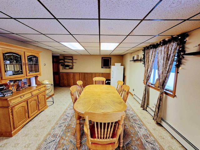 dining area featuring a wainscoted wall, a paneled ceiling, light colored carpet, baseboard heating, and wood walls