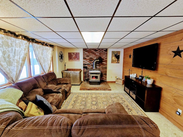 living room featuring carpet floors, a paneled ceiling, wood walls, and a wood stove