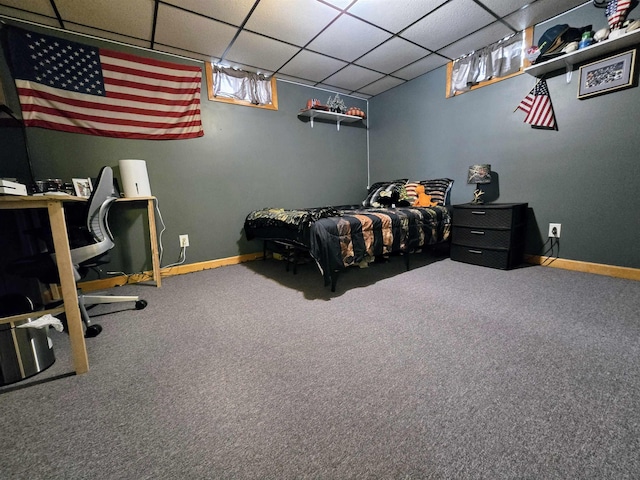 carpeted bedroom featuring baseboards and a drop ceiling