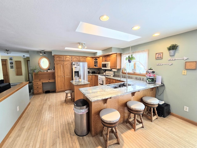 kitchen with a breakfast bar area, white appliances, a skylight, a sink, and brown cabinets