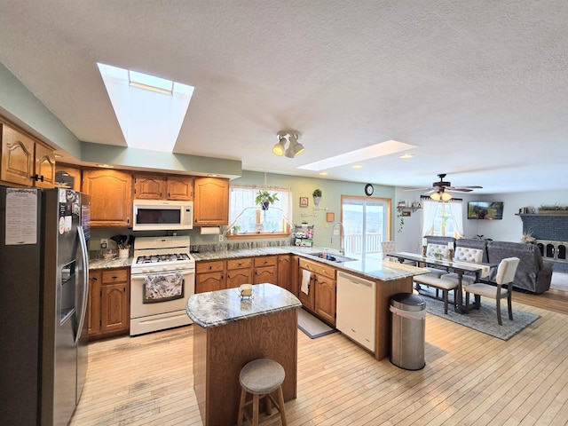 kitchen featuring a skylight, light wood-style flooring, a sink, white appliances, and a peninsula