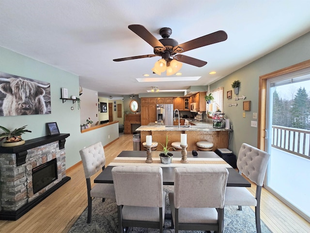 dining space featuring a fireplace, light wood-style flooring, baseboards, and ceiling fan