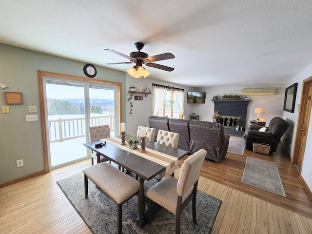 dining space featuring baseboards, a ceiling fan, light wood-style flooring, a wall mounted air conditioner, and a fireplace