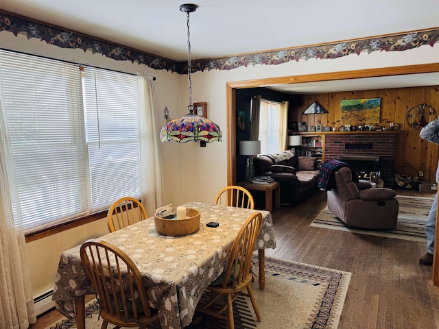 dining room with wood walls, a fireplace, a baseboard heating unit, and wood finished floors