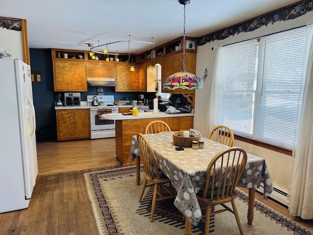 kitchen with under cabinet range hood, a peninsula, white appliances, brown cabinets, and wood-type flooring