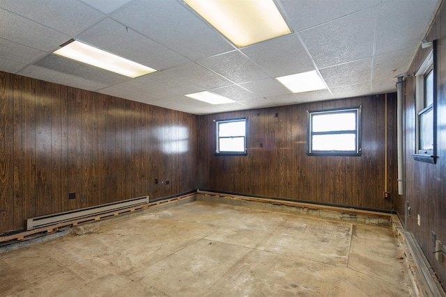 empty room featuring wooden walls, a paneled ceiling, and a baseboard radiator