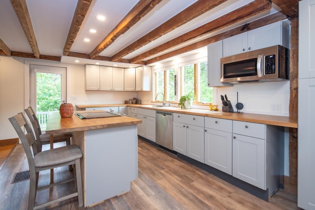 kitchen featuring a healthy amount of sunlight, wood finished floors, wooden counters, stainless steel appliances, and a kitchen bar