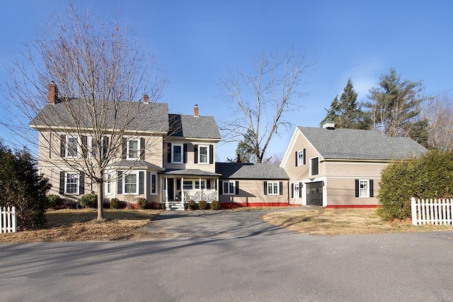 view of front facade with covered porch, driveway, fence, and a garage