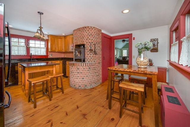 kitchen with decorative light fixtures, light wood finished floors, dark countertops, backsplash, and a kitchen island