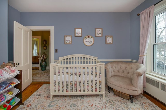 bedroom featuring a nursery area, wood finished floors, and radiator