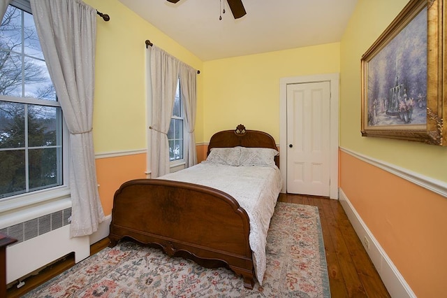 bedroom with radiator heating unit, wood finished floors, a ceiling fan, and baseboards