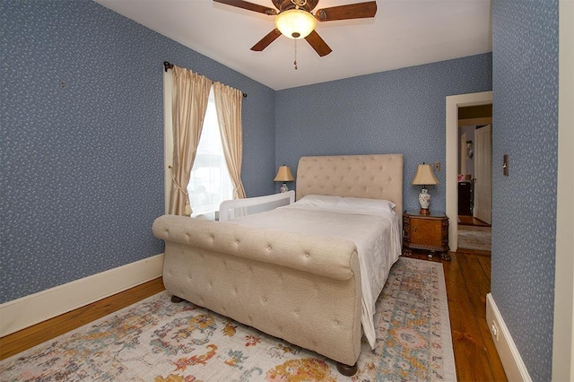 bedroom with wallpapered walls, a ceiling fan, baseboards, and wood finished floors