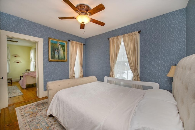 bedroom featuring a ceiling fan, baseboards, hardwood / wood-style floors, and wallpapered walls