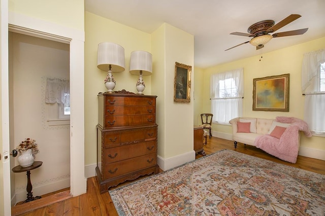 living area with wood finished floors, a ceiling fan, and baseboards