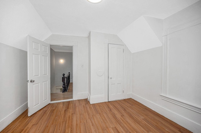 bonus room featuring light wood-type flooring, baseboards, a textured ceiling, and lofted ceiling