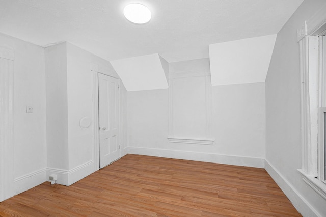 additional living space with lofted ceiling, light wood finished floors, baseboards, and a textured ceiling