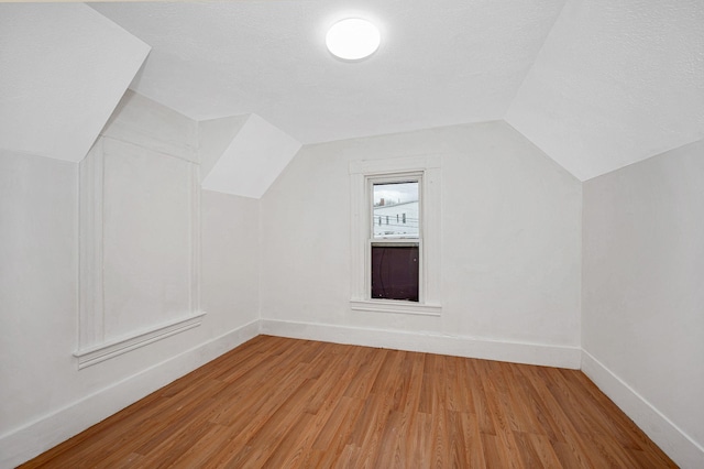 bonus room featuring a textured ceiling, baseboards, vaulted ceiling, and wood finished floors